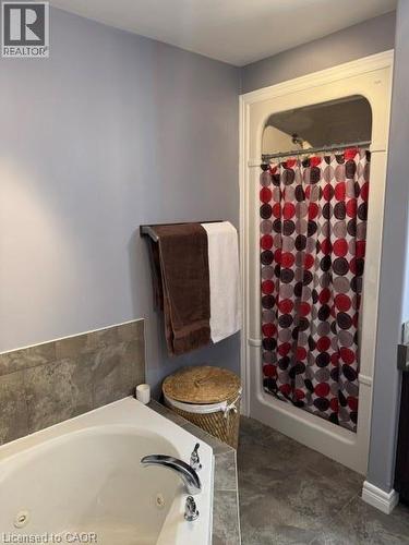 Bathroom featuring a white jetted tub with chrome fixtures, a combination shower/tub unit, and grey large-format tile flooring - 102 Willow Lane, Grimsby, ON - Indoor Photo Showing Bathroom