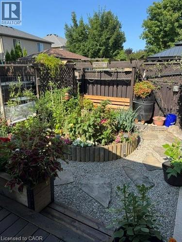 Private backyard retreat featuring a gravel patio with stepping stones, a raised garden bed with timber edging, wood-finish deck, and dark-stained fencing - 102 Willow Lane, Grimsby, ON - Outdoor