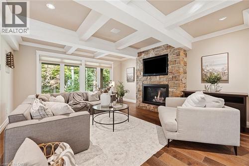 Living area featuring a stone-clad fireplace with built-in media integration, large windows, wood-finish flooring, recessed lighting, and a coffered ceiling - 266 Ferndale Place, Waterloo, ON - Indoor Photo Showing Living Room With Fireplace