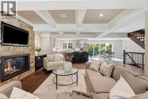 Spacious living area featuring a stone fireplace with a mounted television, wood-finish flooring, a coffered ceiling, and an open-concept layout to the kitchen and dining areas - 266 Ferndale Place, Waterloo, ON - Indoor Photo Showing Living Room With Fireplace