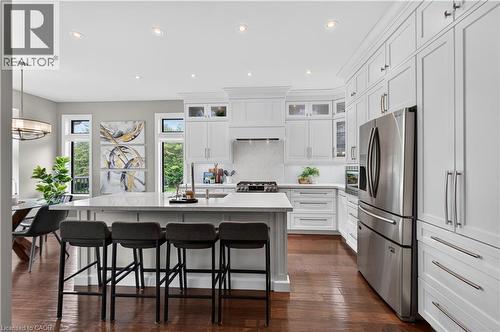 Spacious kitchen featuring white shaker cabinetry, stainless steel appliances, a large center island with seating, recessed lighting, and wood-finish flooring - 2050 15 Side Road, Milton, ON - Indoor Photo Showing Kitchen With Upgraded Kitchen