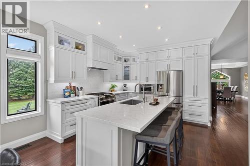 Contemporary kitchen featuring extensive white cabinetry, a large center island with a sink, stainless steel appliances, and wood-finish flooring - 2050 15 Side Road, Milton, ON - Indoor Photo Showing Kitchen With Upgraded Kitchen