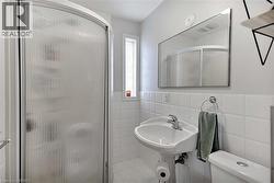 Compact bathroom featuring a curved shower enclosure with frosted glass, a pedestal sink with chrome faucet, a wall-mounted mirror, and white square tile wainscoting - 