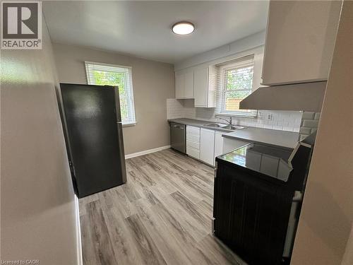 Kitchen featuring light wood-finish flooring, white subway tile backsplash, white cabinetry, a stainless steel sink, and a black range - 20 Lloyd Manor Road, Etobicoke, ON - Indoor Photo Showing Kitchen With Double Sink