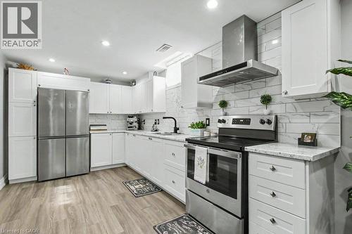 Contemporary kitchen featuring white shaker cabinetry, stainless steel appliances, light granite-finish countertops, subway tile backsplash, and wood-finish flooring - 284 Normanhurst Avenue, Hamilton, ON - Indoor Photo Showing Kitchen With Upgraded Kitchen