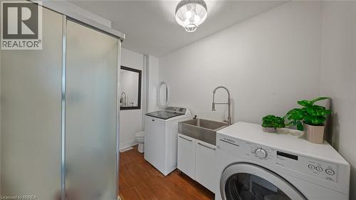 Utility area with wood-finish flooring featuring a double basin utility sink with a high-arc faucet, white cabinetry, and a frosted glass sliding door enclosure - 3211 Highway 3, Jarvis, ON - Indoor Photo Showing Laundry Room