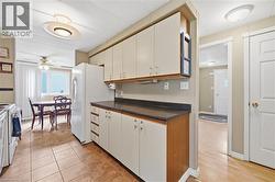 Kitchen featuring tile flooring, white cabinetry with wood accents, dark countertops, and a white refrigerator - 