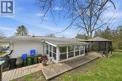 Rear exterior featuring white horizontal siding, a screened-in porch, a wooden deck, a gazebo, and mature trees surrounding the property line - 