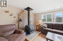 Living area featuring a cast iron wood-burning stove, a stone accent wall with integrated shelving, light wood-finish flooring, and multiple windows - 