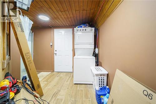 Utility area featuring wood-finish flooring, a wood plank ceiling, and a stacked washer and dryer unit - 7332 Twenty Road E, Glanbrook, ON - Indoor Photo Showing Laundry Room
