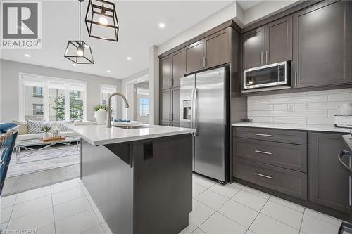 Spacious kitchen featuring an island with sink, dark cabinetry, stainless steel appliances, white subway tile backsplash, and light-toned tile flooring - 542 Boyd Lane, Milton, ON - Indoor Photo Showing Kitchen With Upgraded Kitchen