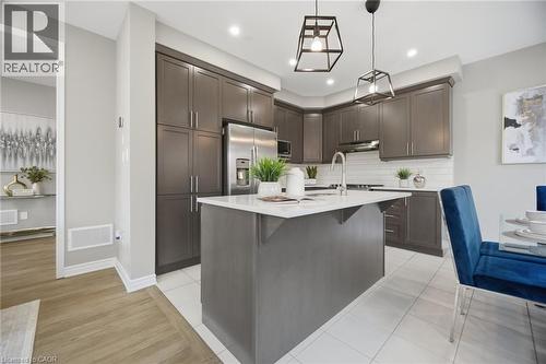 Contemporary kitchen featuring dark wood-finish cabinetry, a large center island with a light-toned countertop, stainless steel appliances, white subway tile backsplash, and recessed lighting - 542 Boyd Lane, Milton, ON - Indoor Photo Showing Kitchen With Upgraded Kitchen