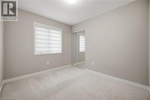 Neutral-toned interior room featuring light-colored carpet, a window with layered shades, and a mirrored sliding closet door - 542 Boyd Lane, Milton, ON - Indoor Photo Showing Other Room