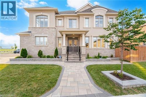 Stucco and stone facade home featuring a prominent arched window, paver walkway, and mature landscaping - 542 Boyd Lane, Milton, ON - Outdoor With Facade