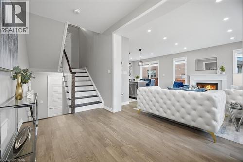 Open-concept living space featuring wood-finish flooring, a contemporary staircase with dark treads, recessed lighting, and a fireplace with a mantel - 542 Boyd Lane, Milton, ON - Indoor With Fireplace