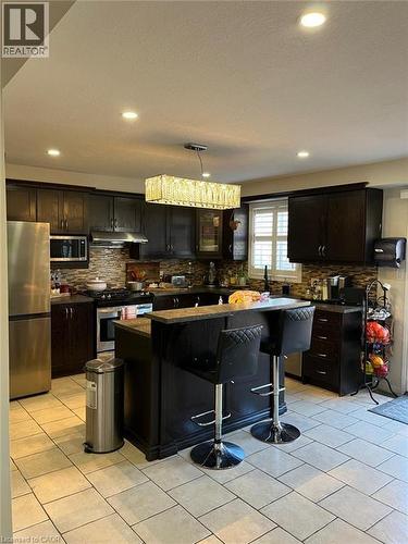 Kitchen featuring dark wood cabinetry, a central island with a raised countertop, stainless steel appliances, and a mosaic tile backsplash - 1367 Upper Paradise Road, Hamilton, ON - Indoor Photo Showing Kitchen