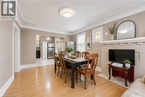 Light wood-finish flooring extending into the background, complemented by a white brick fireplace with a mantle, decorative crown molding, and a visible kitchen area with stainless steel appliances - 74 Royal Avenue, Hamilton, ON - Indoor Photo Showing Dining Room