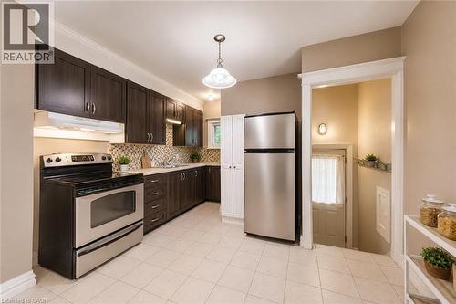 Kitchen featuring dark wood-finish cabinetry, stainless steel appliances, a mosaic tile backsplash, and light-toned tile flooring - 74 Royal Avenue, Hamilton, ON - Indoor Photo Showing Kitchen