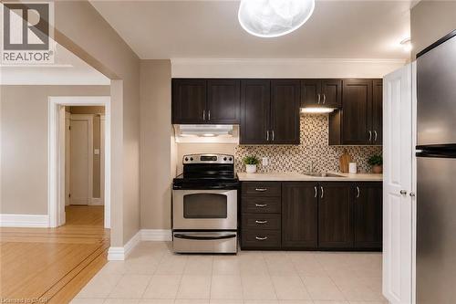 Kitchen featuring dark wood-finish cabinetry, stainless steel appliances, mosaic tile backsplash, and light-toned countertop - 74 Royal Avenue, Hamilton, ON - Indoor Photo Showing Kitchen