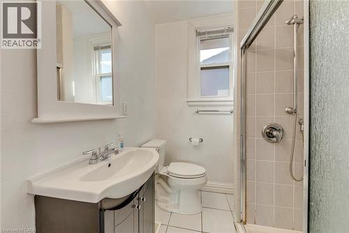 Bathroom featuring a vanity with a white basin and chrome fixtures, framed mirror, white toilet, and a tiled shower with a glass enclosure - 74 Royal Avenue, Hamilton, ON - Indoor Photo Showing Bathroom