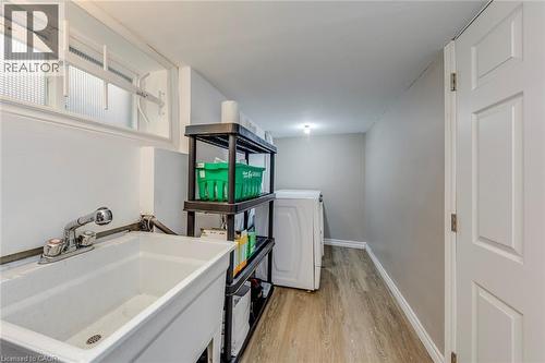 Laundry area featuring a utility sink with a pull-out spray faucet, wood-finish flooring, a white paneled door, and a frosted glass window - 74 Royal Avenue, Hamilton, ON - Indoor Photo Showing Laundry Room