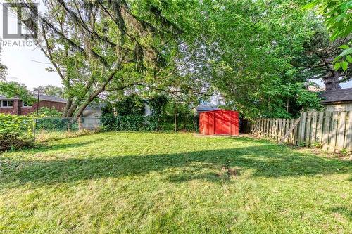 Expansive grassy yard area featuring mature trees providing natural canopy, a red storage shed, chain-link fencing, and a wood privacy fence - 74 Royal Avenue, Hamilton, ON - Outdoor