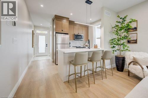 Open-concept kitchen featuring light wood-finish flooring, a white island with an integrated sink, stainless steel appliances, and wood cabinetry - 210 Heritage Drive Unit# Main, Kitchener, ON - Indoor Photo Showing Kitchen With Upgraded Kitchen