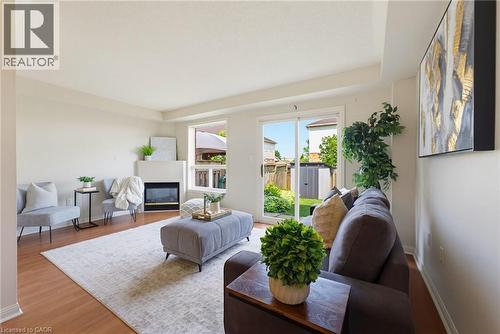 Bright living area featuring wood-finish flooring, a modern fireplace with a white surround, and large windows with backyard visibility - 4425 Peter Drive, Burlington, ON - Indoor Photo Showing Living Room With Fireplace