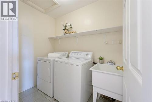 Dedicated laundry space featuring a utility sink, overhead shelving, and tile flooring - 4425 Peter Drive, Burlington, ON - Indoor Photo Showing Laundry Room