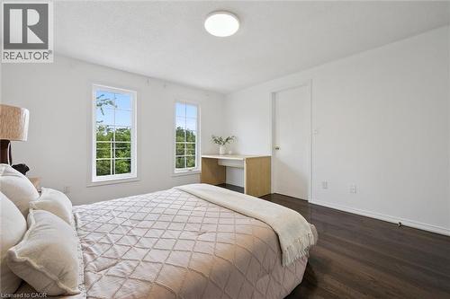 Spacious room featuring two large windows with grid inserts, dark wood-finish flooring, white walls, and a built-in desk alcove - 600 White Elm Boulevard Unit# 9, Waterloo, ON - Indoor Photo Showing Bedroom