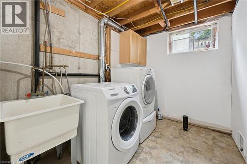 Dedicated laundry area featuring a utility sink, a front-loading washing machine, a stacked dryer, and overhead cabinetry - 600 White Elm Boulevard Unit# 9, Waterloo, ON - Indoor Photo Showing Laundry Room