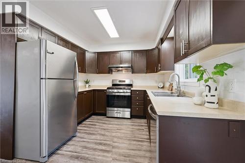 Kitchen featuring dark wood cabinetry, light countertops, wood-finish flooring, stainless steel appliances, and a tile backsplash - 600 White Elm Boulevard Unit# 9, Waterloo, ON - Indoor Photo Showing Kitchen With Double Sink