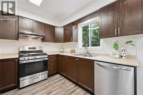 Galley kitchen featuring wood-finish flooring, dark wood cabinetry, and light-toned countertops - 600 White Elm Boulevard Unit# 9, Waterloo, ON - Indoor Photo Showing Kitchen With Double Sink