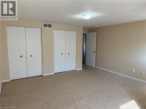 Room featuring neutral carpeting and walls, multiple bi-fold closet doors with brass-finish hardware, white baseboards, and a semi-flush ceiling light fixture - 11 Hackberry Street Unit# 1, Kitchener, ON - Indoor Photo Showing Other Room