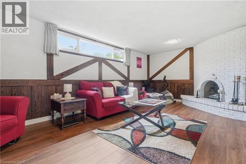 Recreation room featuring wood-finish flooring, a white-painted brick fireplace with an arched opening, and a wood-paneled accent wall with decorative beams - 76 Lower Canada Crescent, Kitchener, ON - Indoor