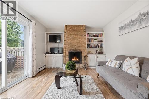 Living area featuring a brick-faced fireplace with a gas insert, wood-finish flooring, and a sliding glass door to an outdoor patio - 76 Lower Canada Crescent, Kitchener, ON - Indoor Photo Showing Living Room With Fireplace