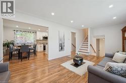 Open-concept living space featuring wood-finish flooring, recessed lighting, a staircase with wood railings, and an archway opening to a kitchen with white cabinetry and a tiled backsplash - 