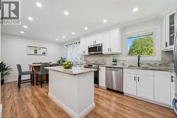 Kitchen featuring white shaker cabinetry, stainless steel appliances, a center island with a stone countertop, and wood-finish flooring - 
