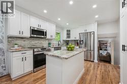Contemporary kitchen featuring white cabinetry, stainless steel appliances, a center island with stone countertop, wood-finish flooring, and recessed lighting - 