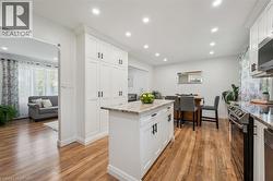 Bright kitchen featuring white shaker cabinetry, stainless steel appliances, a center island with countertop, and wood-finish flooring - 