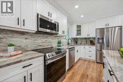 Kitchen featuring white shaker-style cabinetry, stainless steel appliances, marbled countertops, a matching full-height backsplash, and wood-finish flooring - 76 Lower Canada Crescent, Kitchener, ON - Indoor Photo Showing Kitchen With Upgraded Kitchen