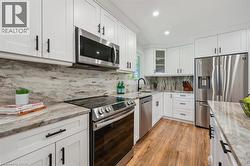 Kitchen featuring white shaker-style cabinetry, stainless steel appliances, marbled countertops, a matching full-height backsplash, and wood-finish flooring - 