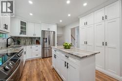 Contemporary kitchen featuring white cabinetry with black hardware, stainless steel appliances, wood-finish flooring, a central island with countertop, and recessed lighting - 