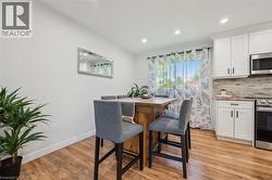Open-concept kitchen and dining area featuring wood-finish flooring, recessed lighting, and white cabinetry with dark hardware - 