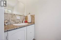 Bathroom vanity featuring a drop-in sink, dual-handle faucet, granite-finish countertop, and white cabinetry - 