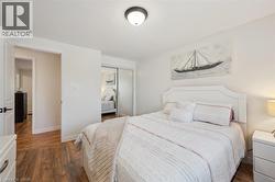 Bedroom featuring wood-finish flooring, a white headboard, a semi-flush mount ceiling light, and mirrored sliding closet doors - 
