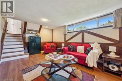 Recreation room featuring wood-finish flooring, white paneled walls with wood beam accents, and a built-in staircase with a wood handrail - 