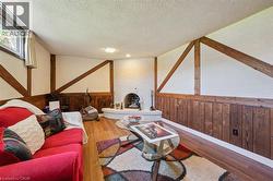 Recreation room featuring wood-finish flooring, white brick fireplace, wood paneling, exposed wood beams, and a window providing natural light - 