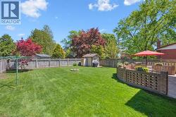 Expansive lawn area with a perimeter wood fence, mature trees, a brick patio, and a curved brick privacy wall - 