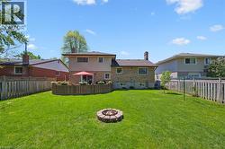 Expansive backyard featuring a manicured lawn, a circular stone fire pit, and a wooden privacy fence - 